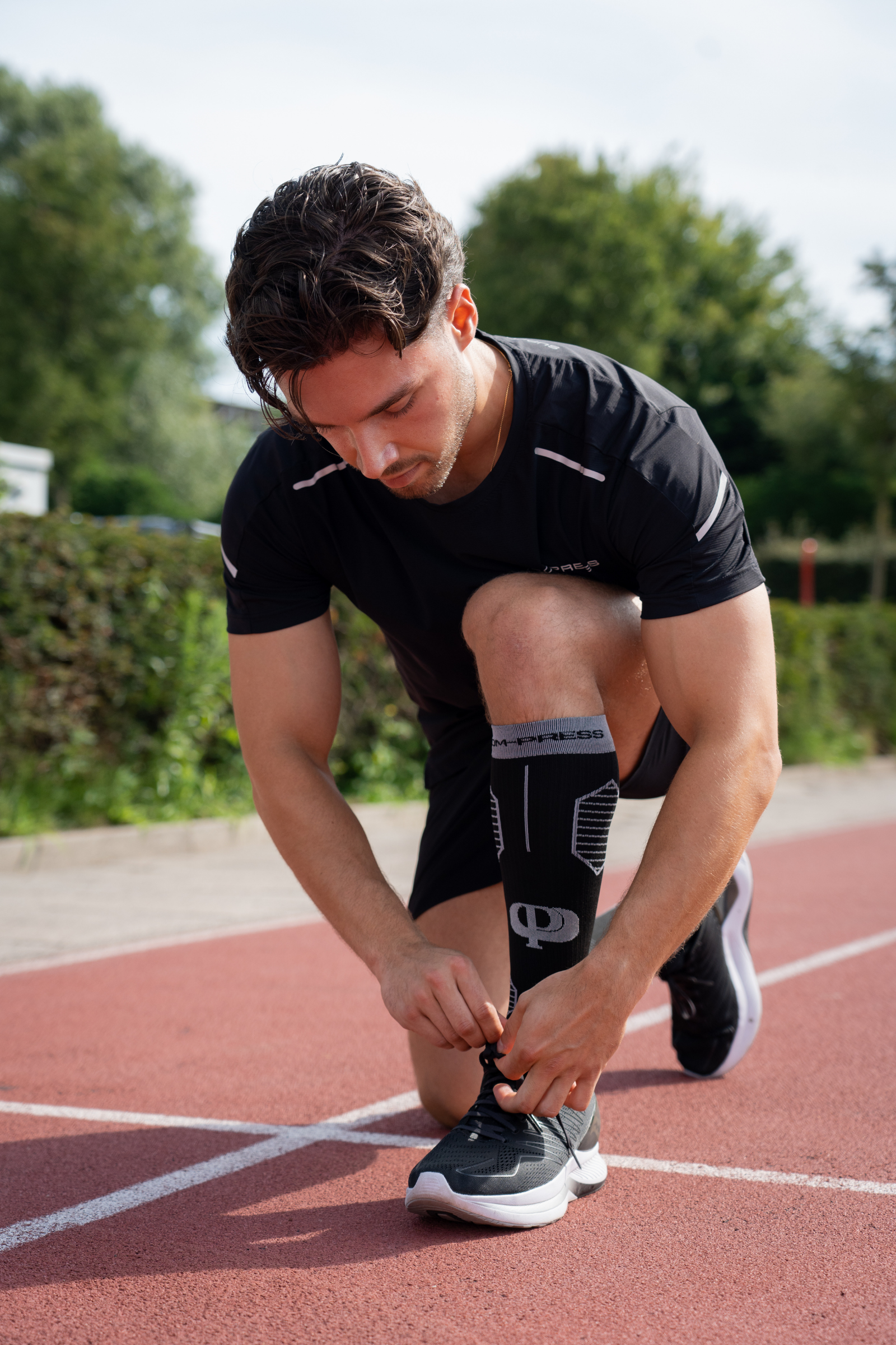 Man tying his running shoes on a track with trees in the background
