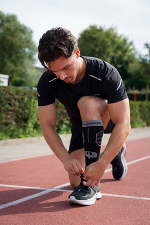 Man tying his running shoes on a track with trees in the background