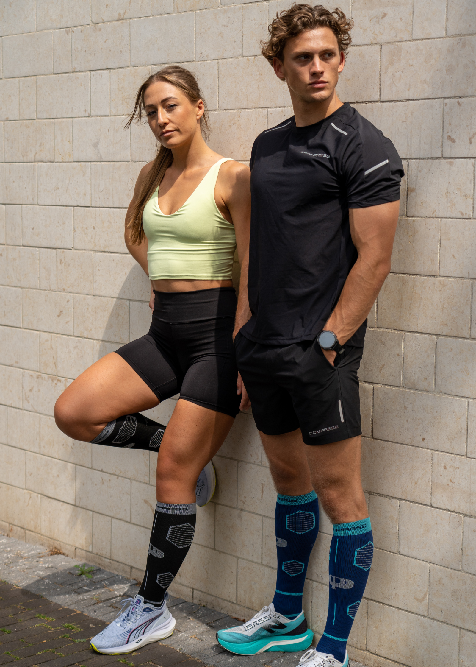 Two people in athletic wear standing against a brick wall.