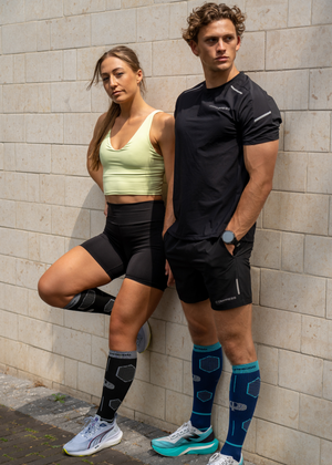 Two people in athletic wear standing against a brick wall.